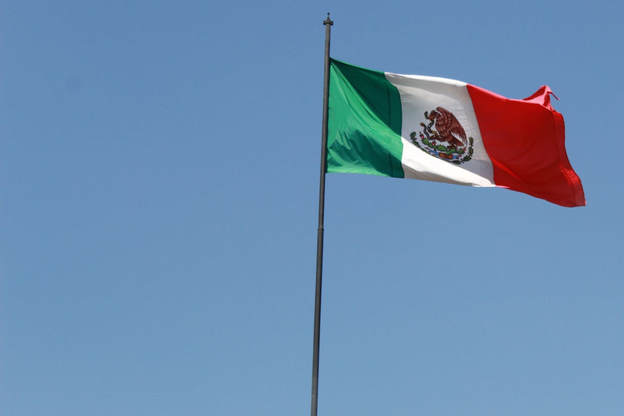 gallery-6 The Mexican flag proudly waves against a clear blue sky in Mexico City, CDMX.